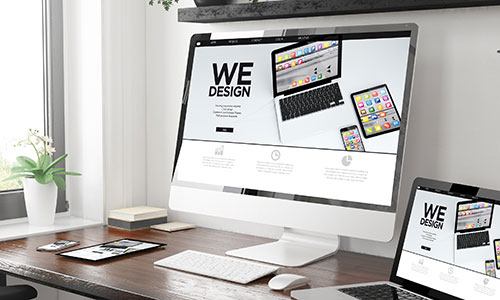 Arbeitsplatz mit großem Monitor und Laptop, beide mit Webdesign-Oberfläche.